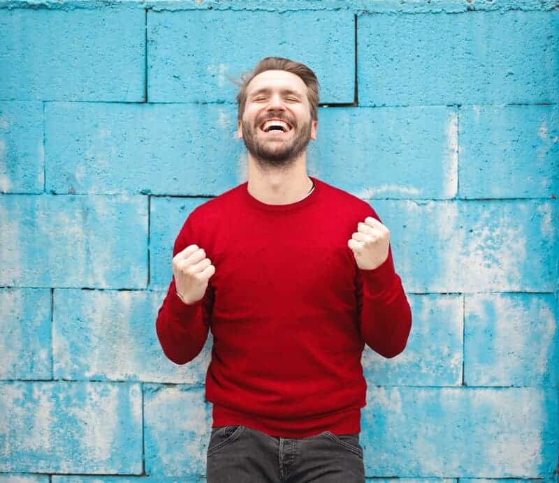 Šťastný muž v červenom svetri pred svetlomodrou stenou